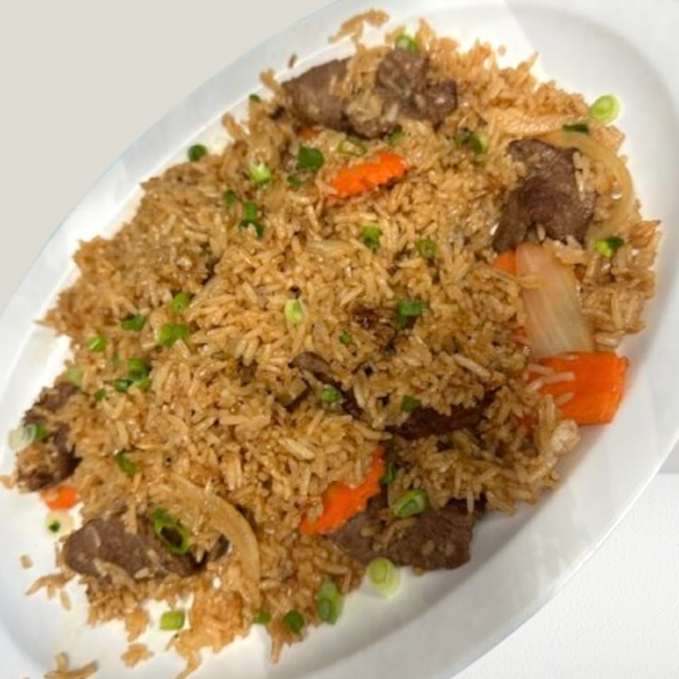 Beef fried rice with carrots, onions, and green onions on a white oval plate.