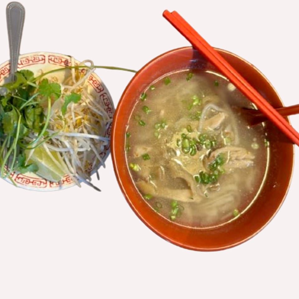 A bowl of Pho Lena's Vietnamese pho with chopsticks, and a side of bean sprouts, cilantro, and lime.